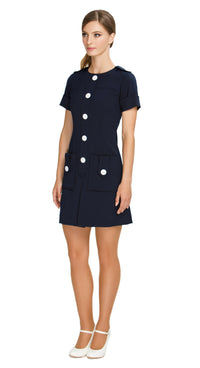 Elevate your wardrobe with our Fitted Sixties Style Dress; perfect for work or play. This dress boasts a uniformed aesthetic, flattering panel craftsmanship, and decorative button torso detailing. With deep skirt pockets, a front pleat, and decorative button-down shoulder tabs, it combines elegance and functionality effortlessly. 