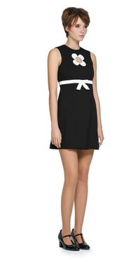 Autumn, mod style little black dress with a slight A-line, rounded neckline, detailed with a carefully sewn floral cut-out on the torso, accented by a contrasting high waist-level bow. Shown here as sleeveless, but available with alternative sleeve and hem lengths to suit preference. A simple, fun, and striking dress that's easy to reach for and pairs well with both heels and pumps. 