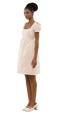 Woman wearing a rose coloured 1960s inspired babydoll dress  on a white background.