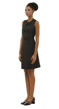 Woman wearing a black sleeveless dress with bow details on a white background