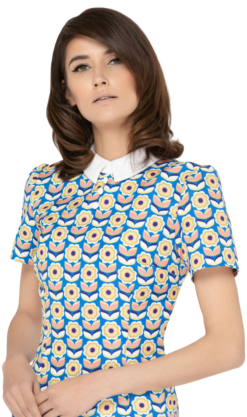 This classic, fitted sixties style spring floral dress produced in a luxury French mill weave in royal blue, pink, white, mustard yellow and navy-blue tones, with a classic stand up collar and short slightly puffed sleeves. It is designed with a zippered back closure for easy wear. The intricate detailing and exquisite craftsmanship make it a stunning piece. Perfect for a warm spring day, this dress is both stylish and comfortable.