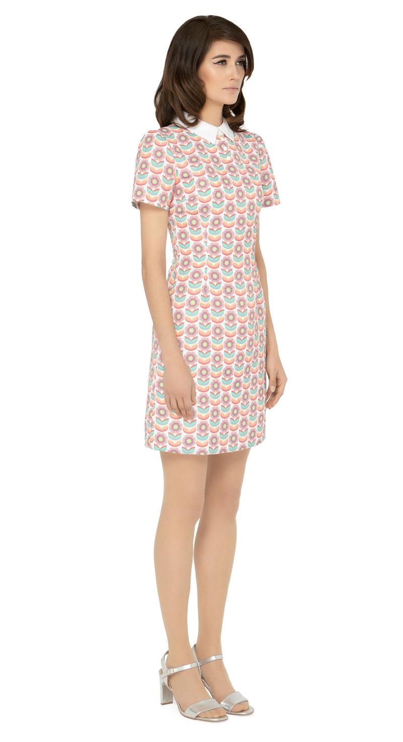 This classic, fitted sixties style spring floral fabric dress produced in a luxury French mill weave in white, peach, red, green, blue and yellow tones, with a classic stand up collar and short slightly puffed sleeves. It is designed with a zippered back closure for easy wear. The intricate detailing and exquisite craftsmanship make it a stunning piece. Perfect for a warm spring day, this dress is both stylish and comfortable.